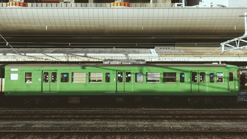 a green train traveling past a tall white building