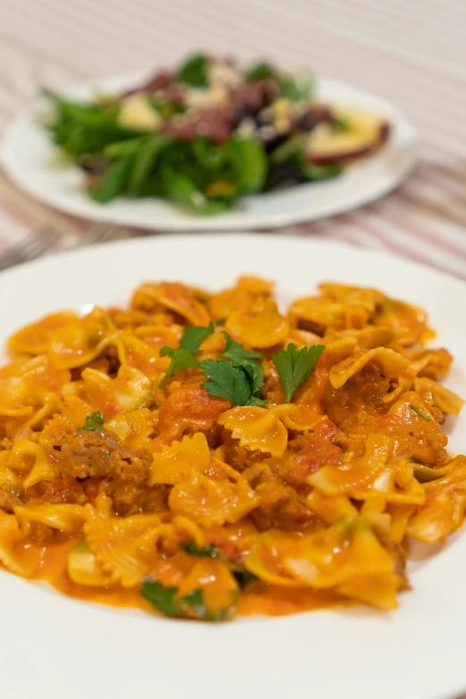 a pasta dish sits on a plate, beside another plate full of vegetables and meat