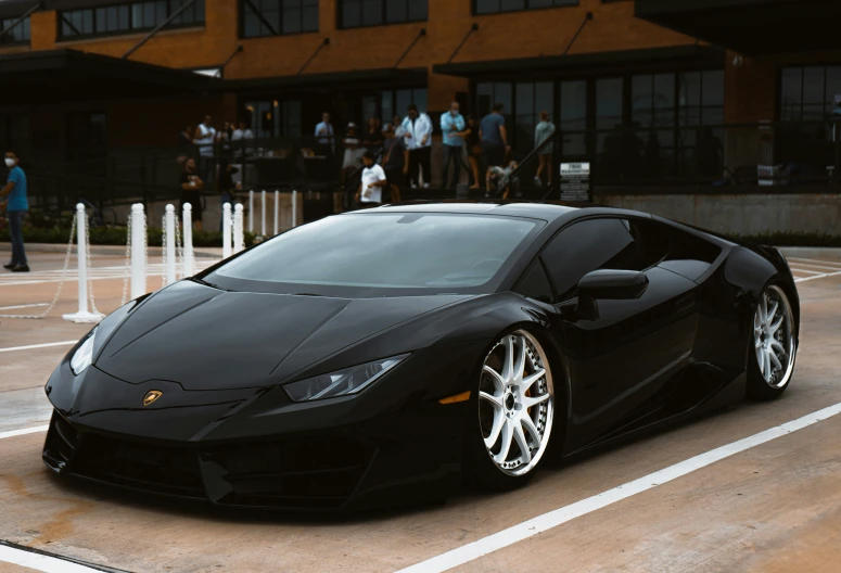 black car with white rims sits parked in front of people