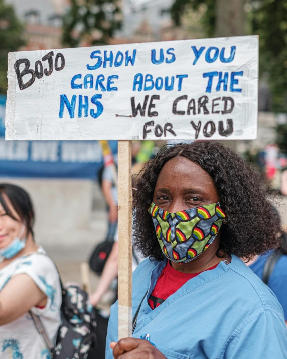 a woman wearing a colorful mask standing in the street holding a sign