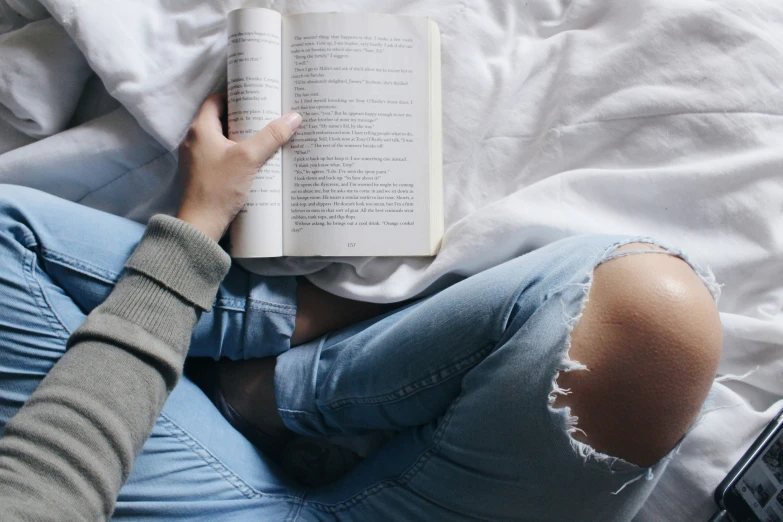 a girl is laying on a bed holding an open book