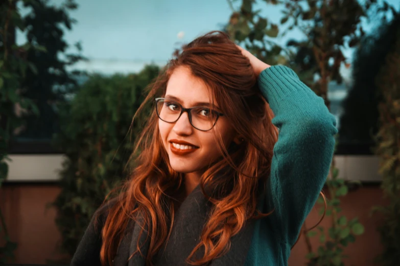 a young woman wearing glasses posing with her hand on her hair