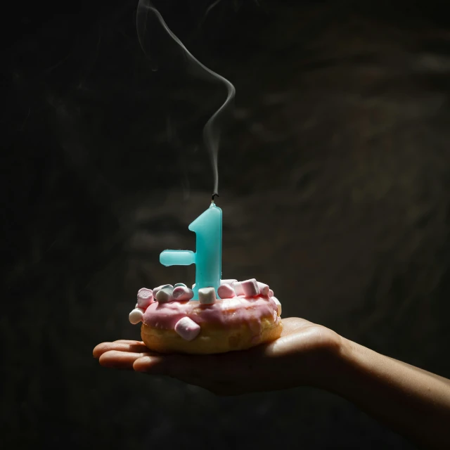 person holding cupcake with one candle lit in it