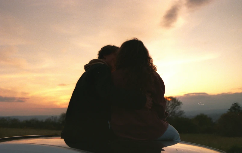 a couple kissing on the hood of a car at sunset