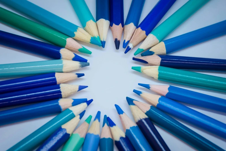 a group of blue and green pencils with one light colored pencil facing the camera