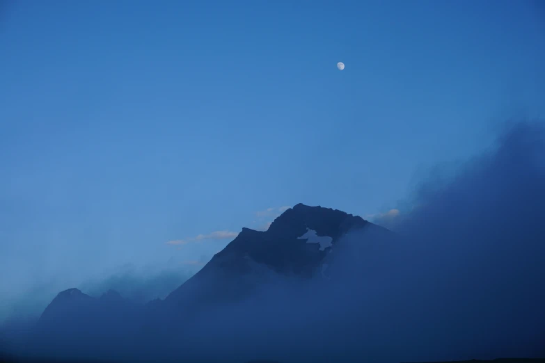 an illuminated full moon above mountains with fog