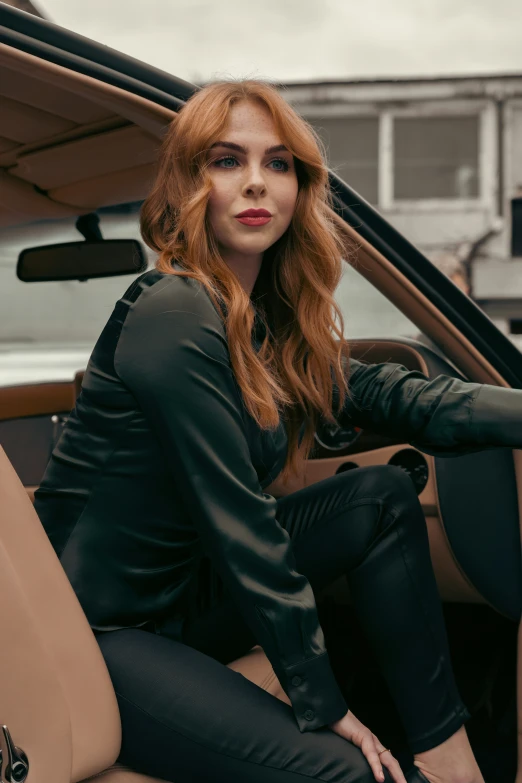 red headed woman in leather outfit sitting inside a luxury vehicle