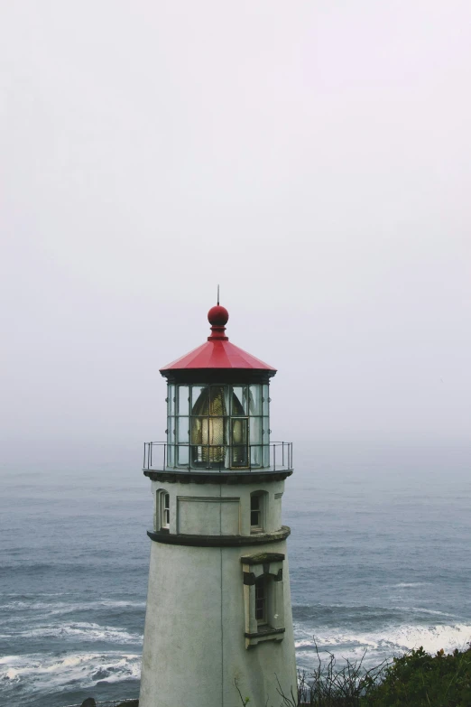 a red and black lighthouse on a hill with a foggy ocean behind it