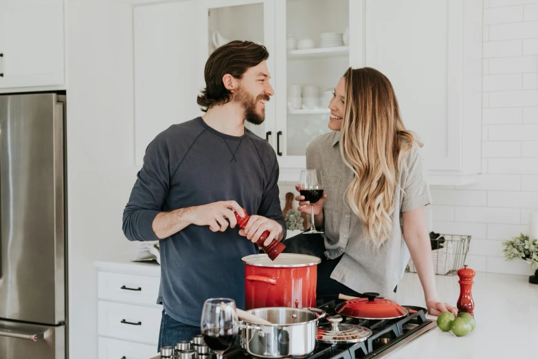 a man and woman standing together in the kitchen with vegetables and sauce