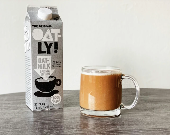 a glass coffee cup next to a carton of oat latte