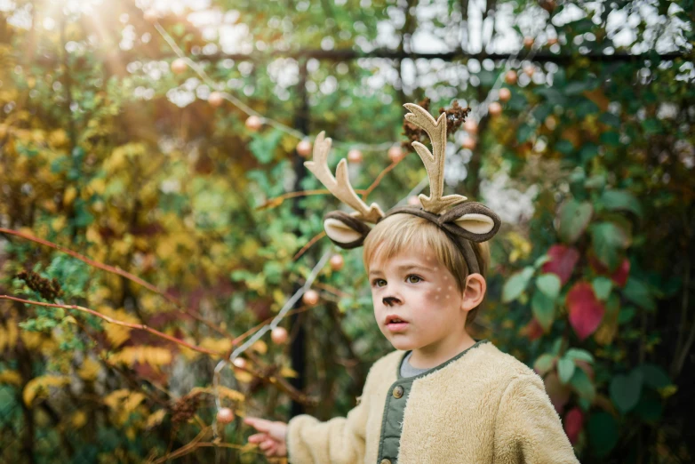 a boy is holding onto a plant while wearing a deer headpiece