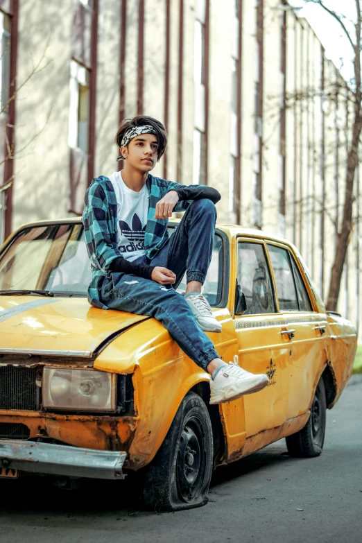 young man sitting on the hood of a car that was burnt