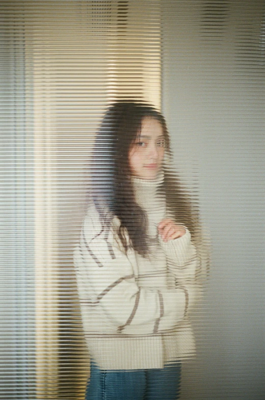 a woman posing in front of blinds with her hands folded around her neck