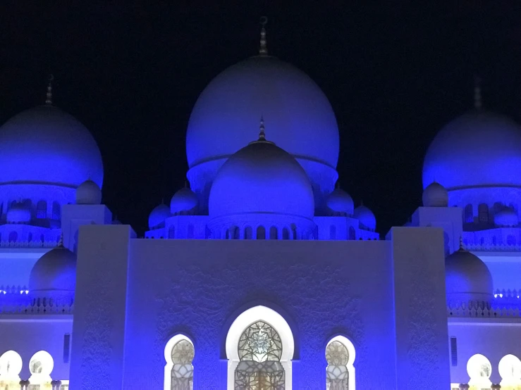 a blue lit white building with three clock in front of it