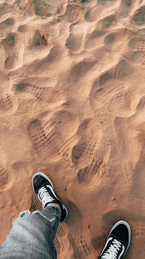 a persons feet standing on a brown colored beach sand