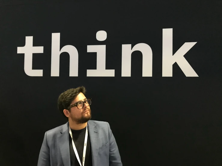 a man with glasses standing in front of a think sign