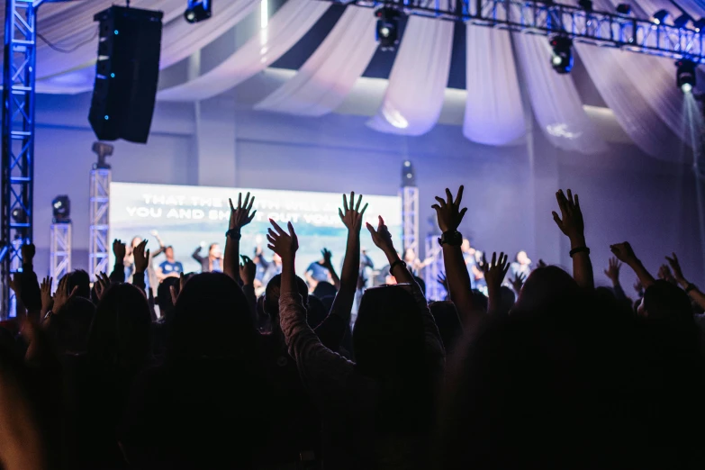 a crowd of people raising their hands to see a speaker