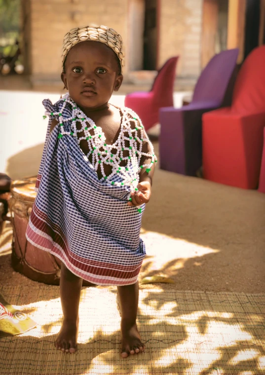 a small child in a blue dress, wearing a head piece and with a chain around his neck