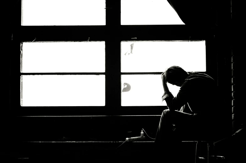 a man sitting in front of a window looking out the window