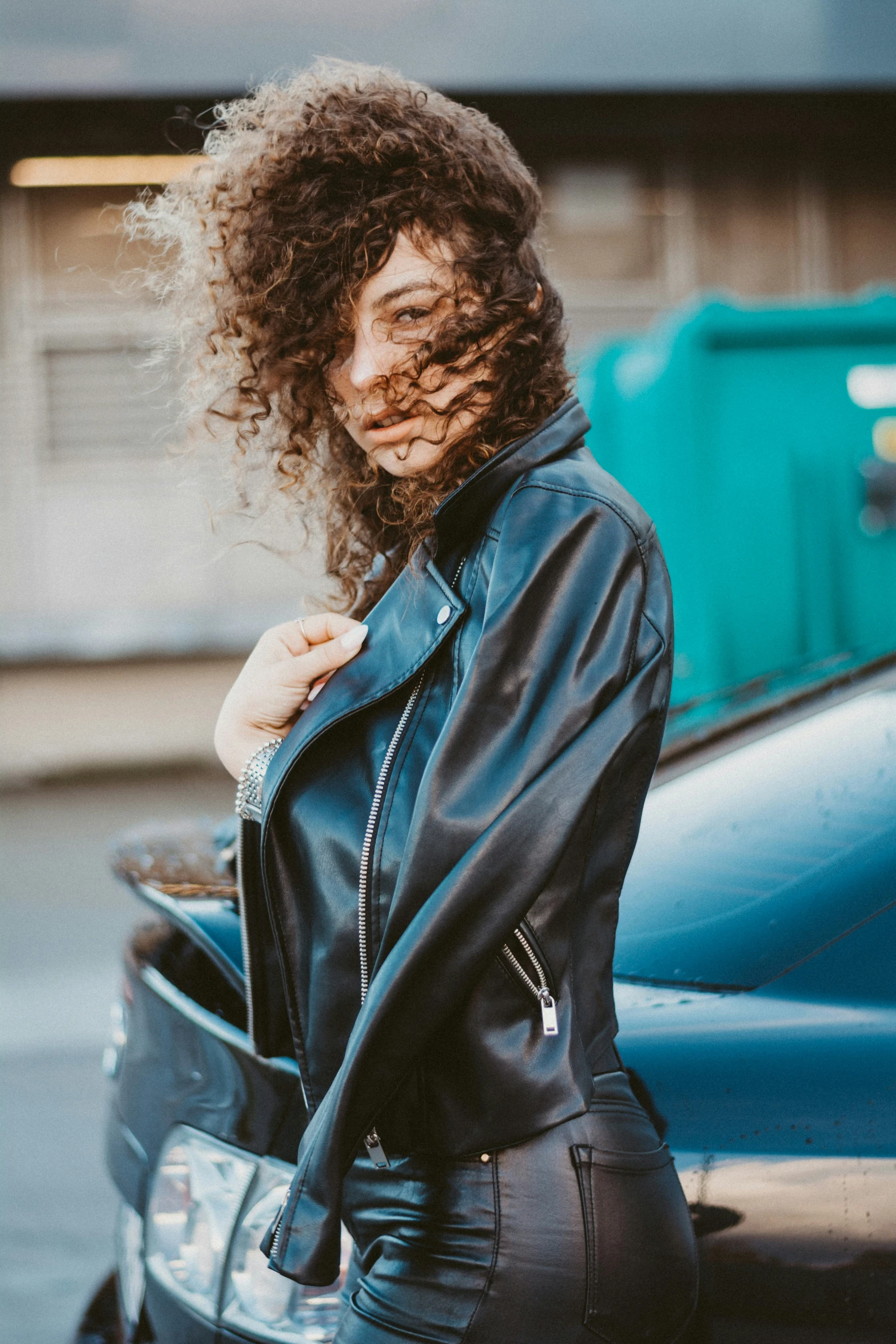 a woman in a black leather jacket is leaning on her blue car