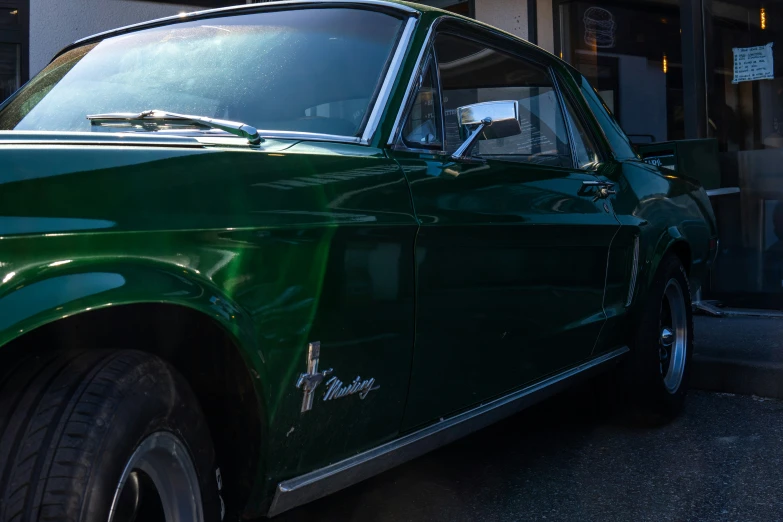 an old green car sits parked in front of a building