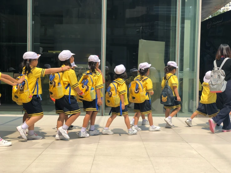 several school girls walking in line with bags and yellow jackets