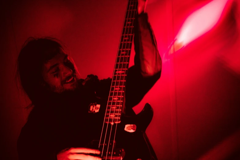 man holding onto red and black guitar against wall