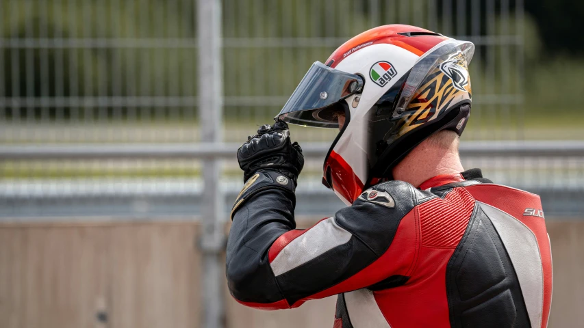 a man wearing a racing suit and a helmet holds his fist up