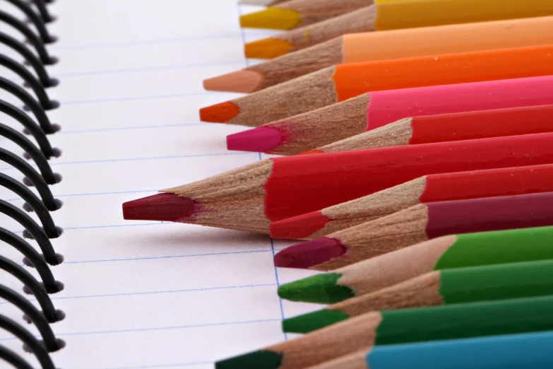 several colored pencils sitting on top of lined up paper