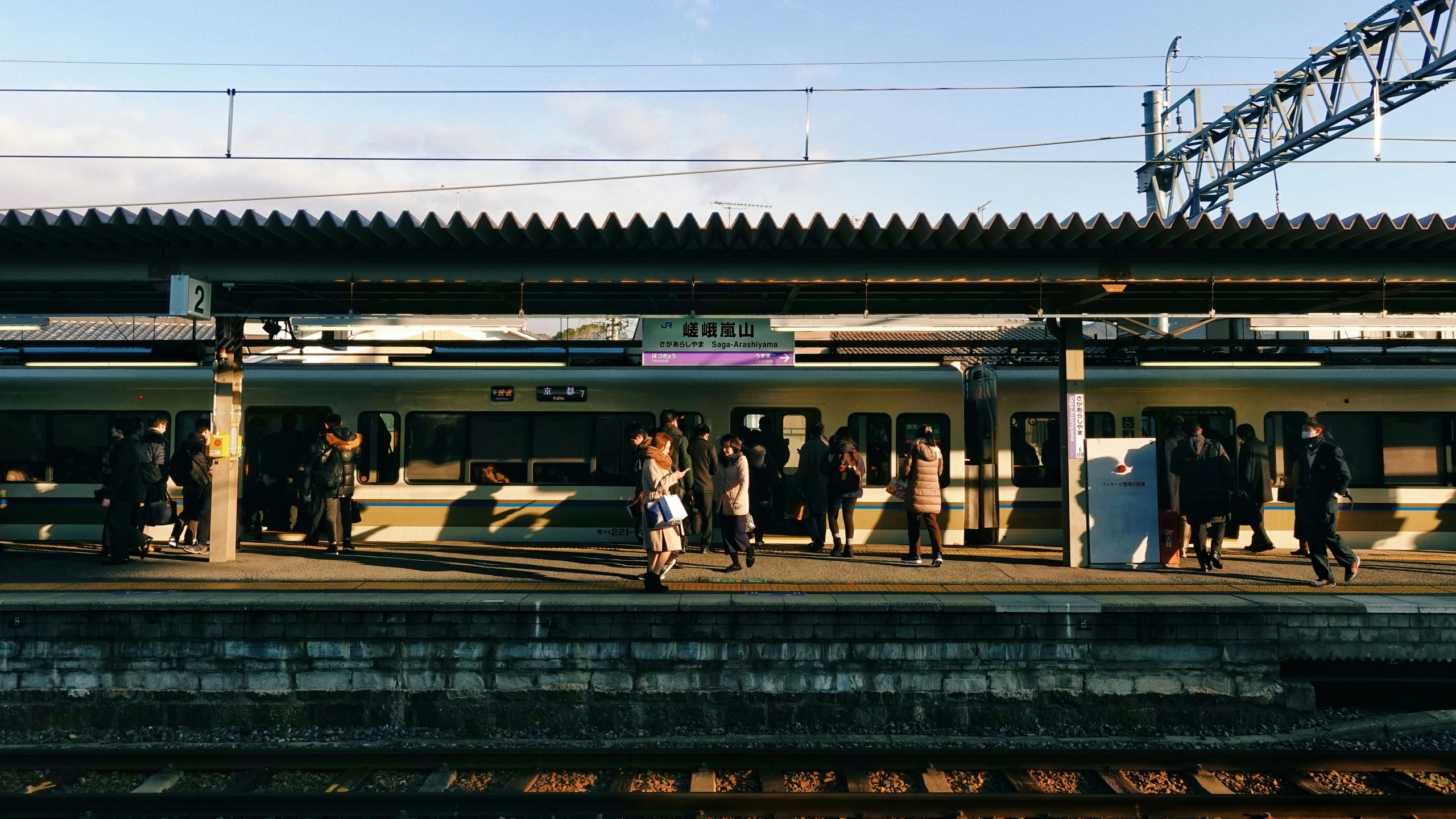 several people are standing at the station waiting for their train