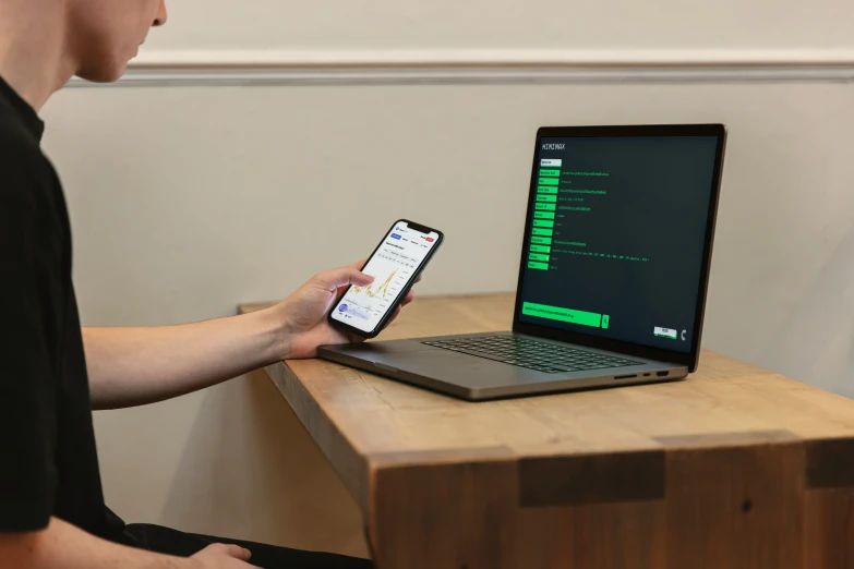 a young man is holding two cell phones while typing on a laptop