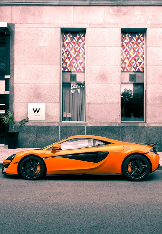 an orange sports car parked on the street in front of a building