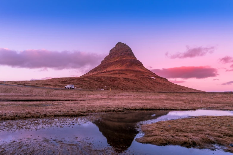 a mountain with water running down it with a truck parked in the grass near it