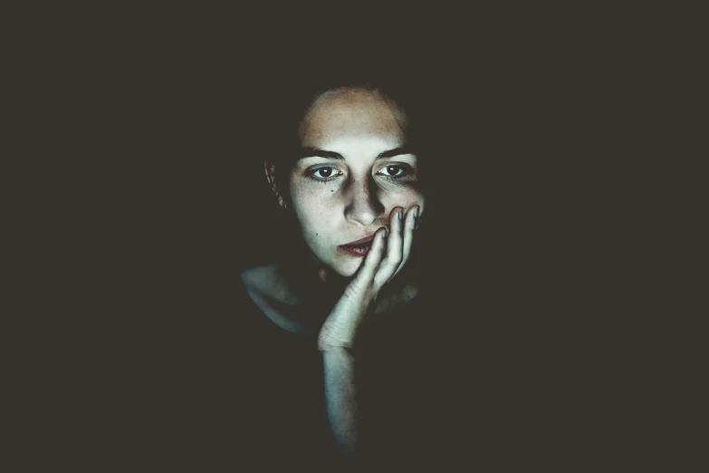 a young person with their hand to their face in the dark