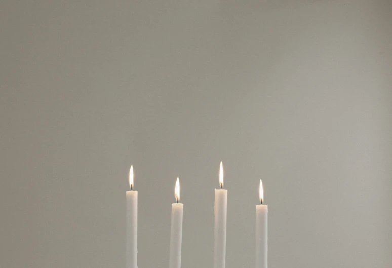 five lit candles stand on a plate and sit in front of a plain gray wall