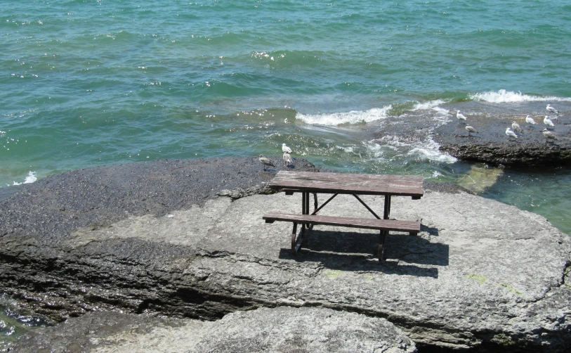 a picnic table sitting on top of a rock near the ocean