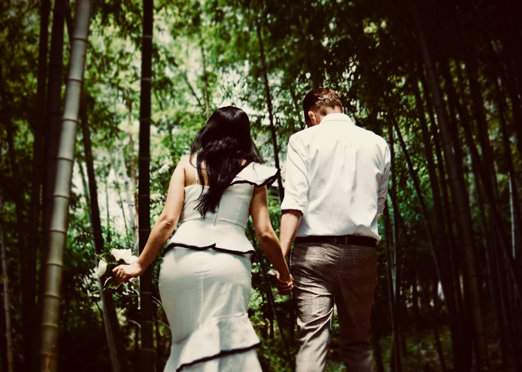 a pregnant bride and groom walk through an area of trees