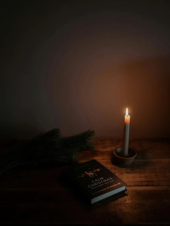 a lit candle is on the table beside a book