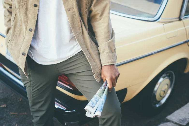 a man with a newspaper and a jacket leaning against a car