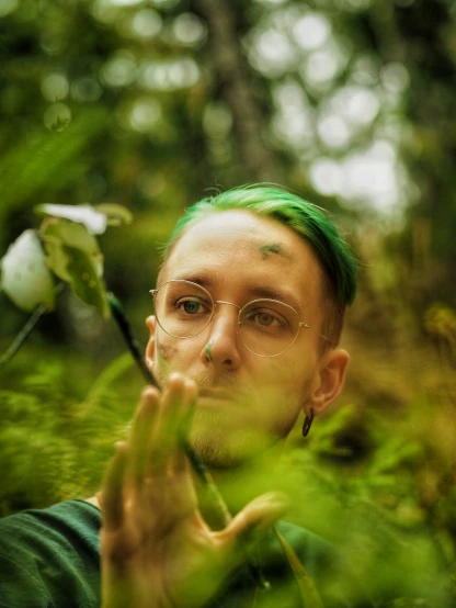 a guy with green hair and glasses holding soing up