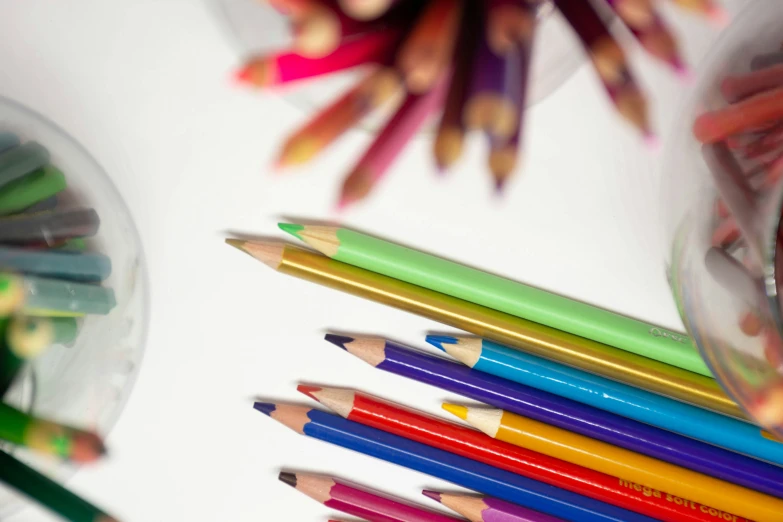 many colored pencils on the surface beside a cup and container