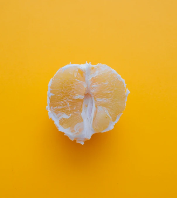 a peeled orange on a yellow background with a few pieces removed