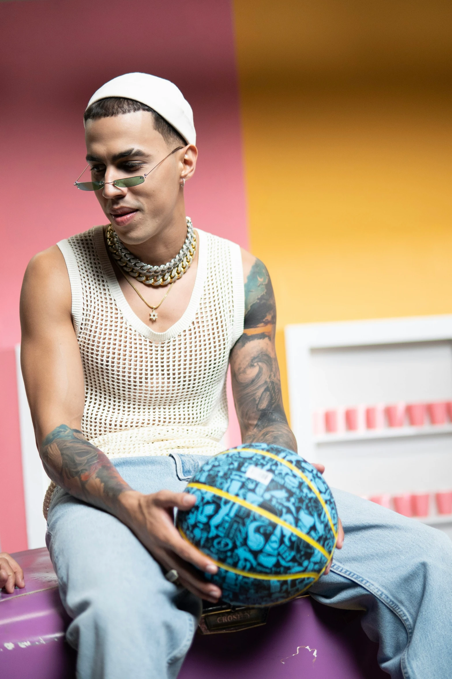 tattooed man in white shirt sitting on pink and yellow building