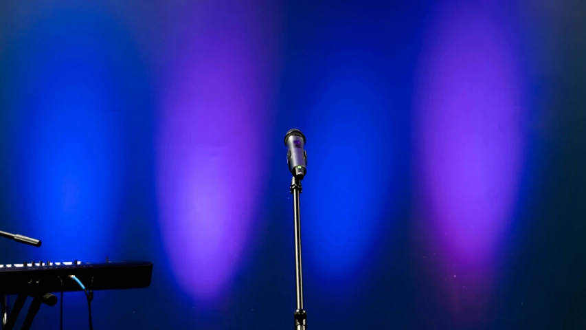 a microphone stands against a blue background with speaker equipment