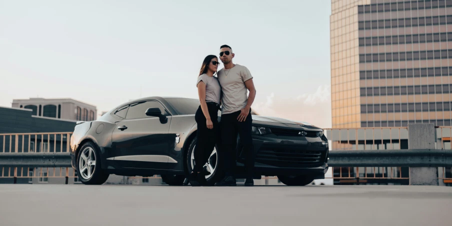 couple standing beside a silver car by the water