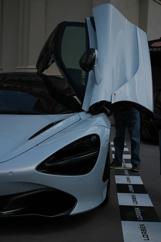 the man inspects the front bumper of a white sports car