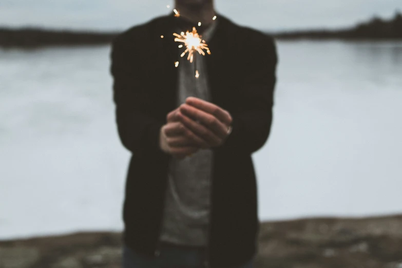 the man is standing near a body of water holding his sparkler