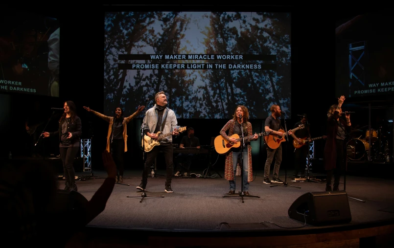 a group of people playing guitars in front of a large screen