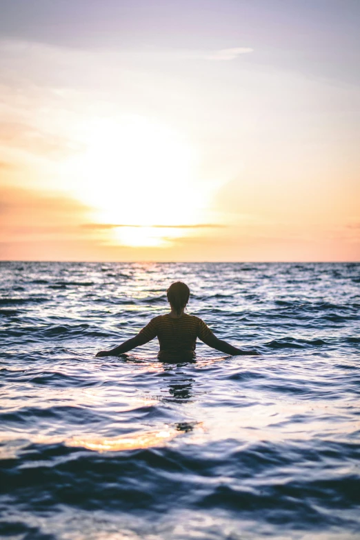 the man stands in the water with his arms stretched out as the sun goes down