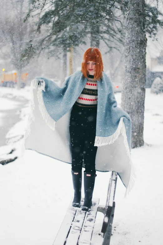 a woman standing on a park bench covered with a blanket